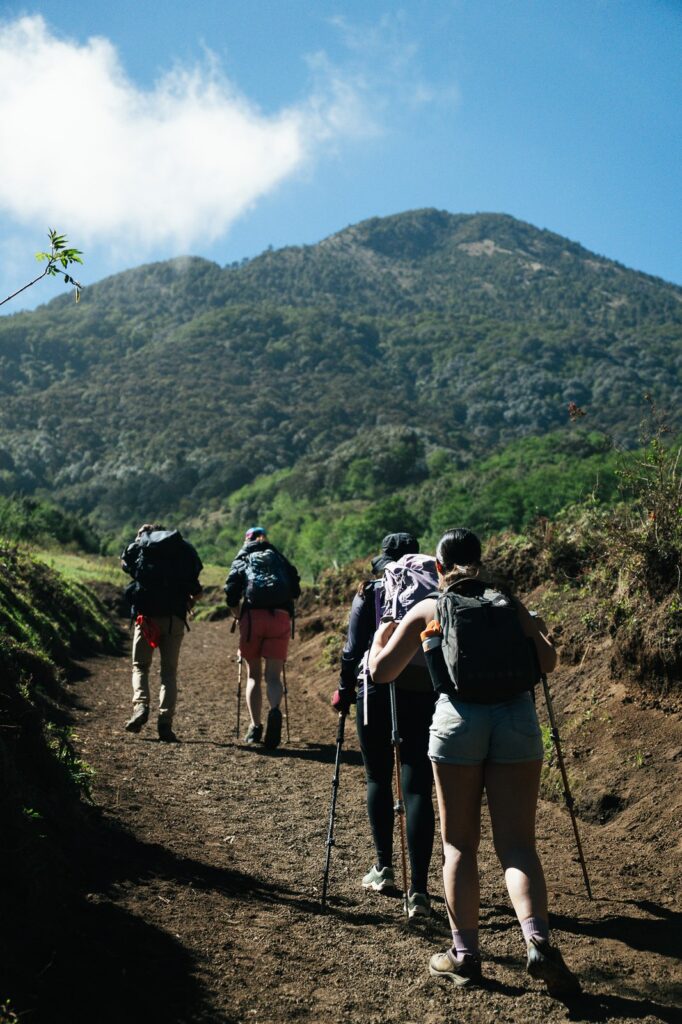Hikers ascend Acatenango Volcano on a dirt trail, trekking uphill with backpacks and hiking poles.