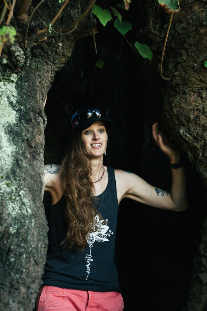 Woman in tank top and hat standing in cave entrance. Namaste text on shirt.