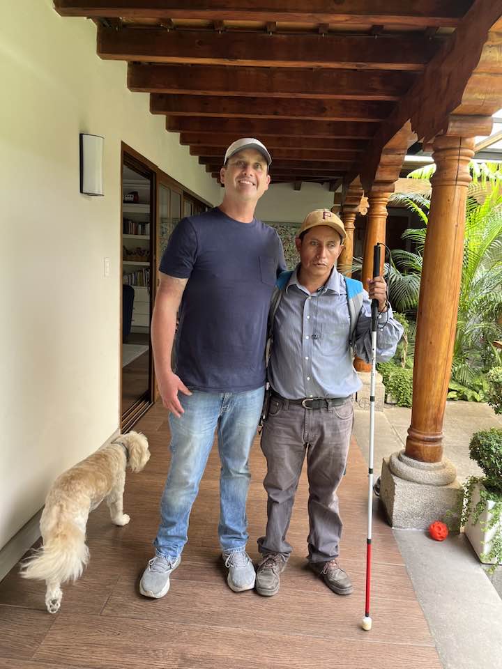 CoPilots Project: Two men and a dog stand on a porch, one man with a white cane.