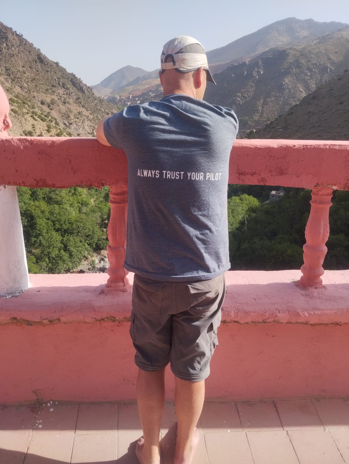 Man wearing a t-shirt that says "Always Trust Your Pilot" looks out at a mountain landscape.