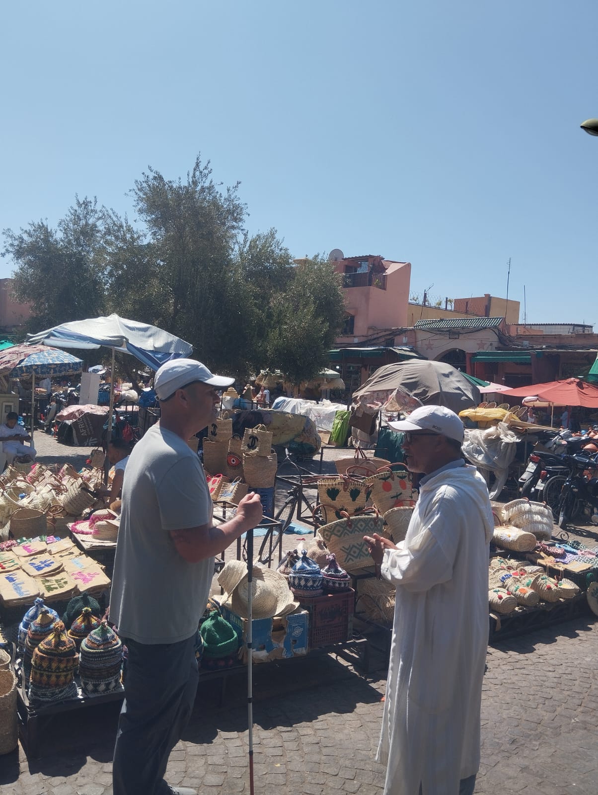 Two men talking at a Moroccan market stall selling woven baskets and hats.