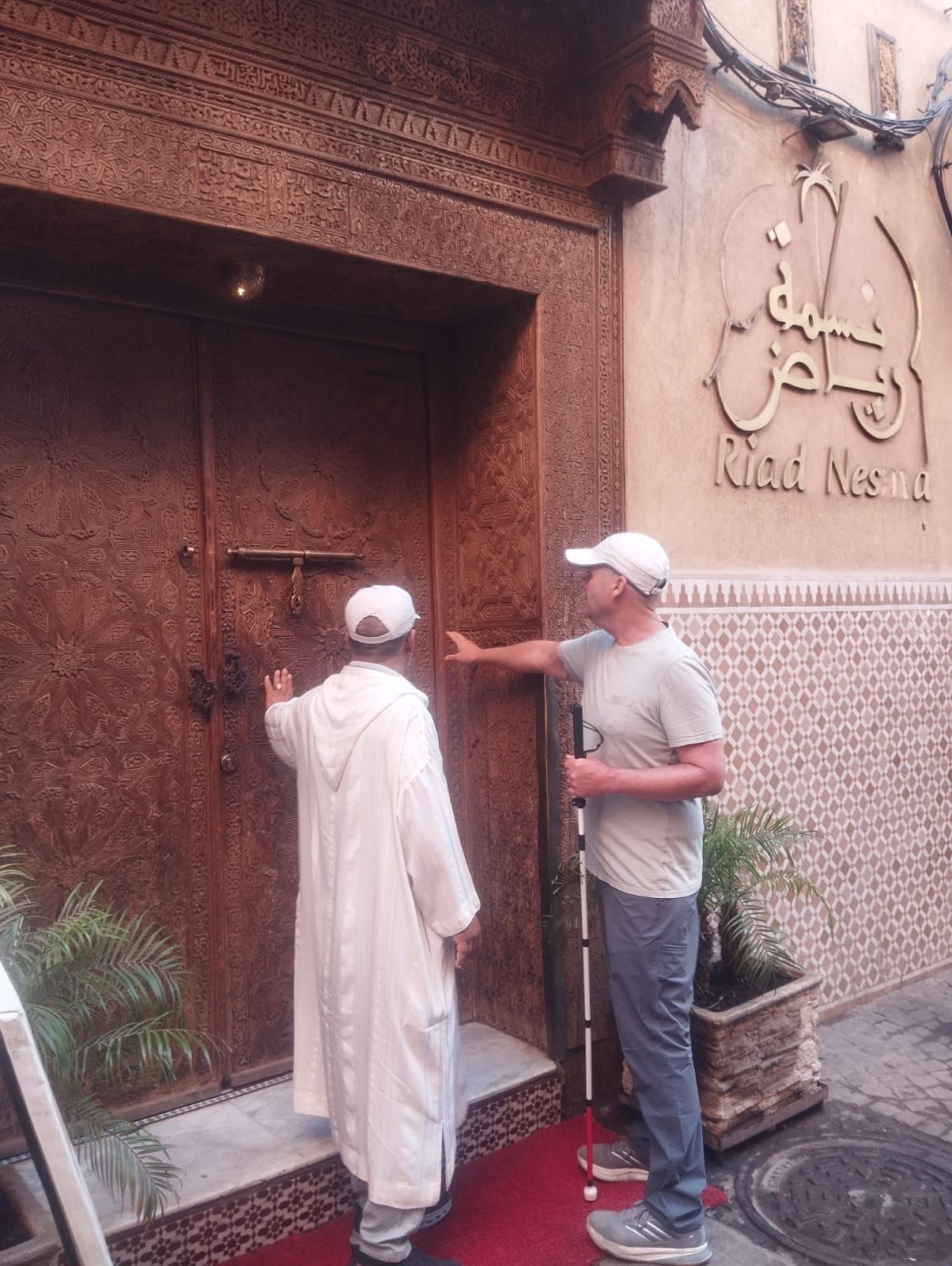 Two men, one in a white djellaba, stand before a carved wooden door at Riad Nesma.