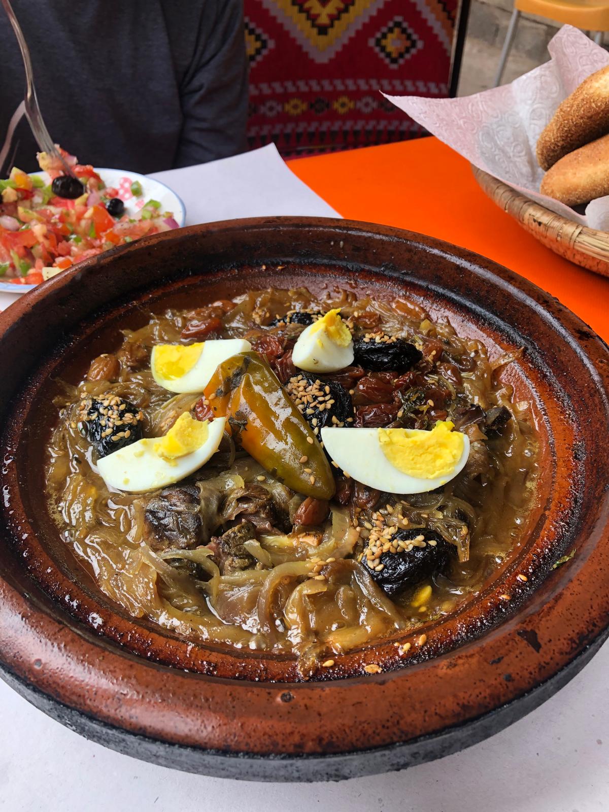 Moroccan lamb tagine with prunes, eggs, and green peppers in a clay pot.