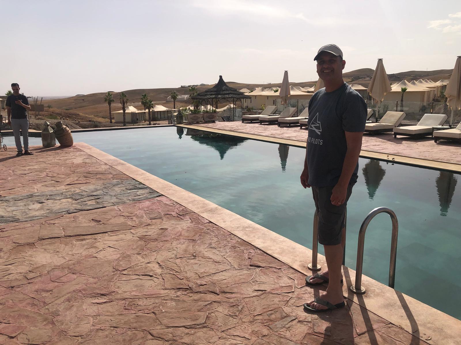 Man in a cap and shorts by a luxury infinity pool at a desert resort