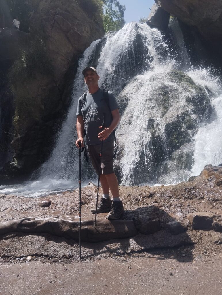 Man with trekking poles at base of a waterfall