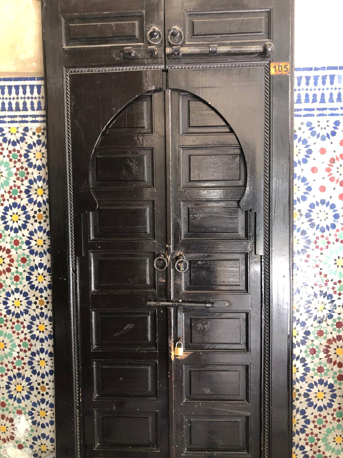 Dark wooden double doors with intricate geometric tilework and a brass padlock.