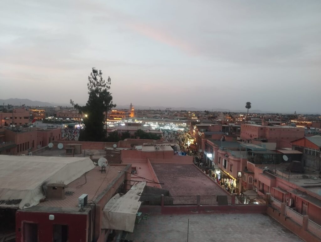 Rooftop view of Jemaa el-Fnaa square in Marrakech at dusk, with market stalls and crowds.