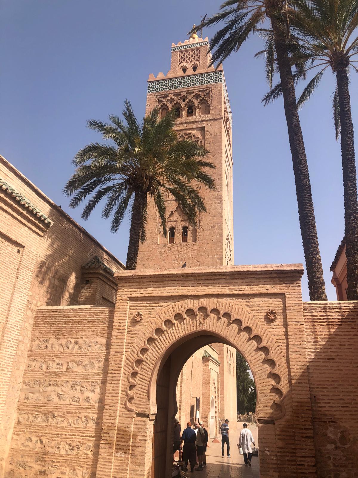 Koutoubia Mosque minaret in Marrakech, Morocco, with palm trees and ornate archway.
