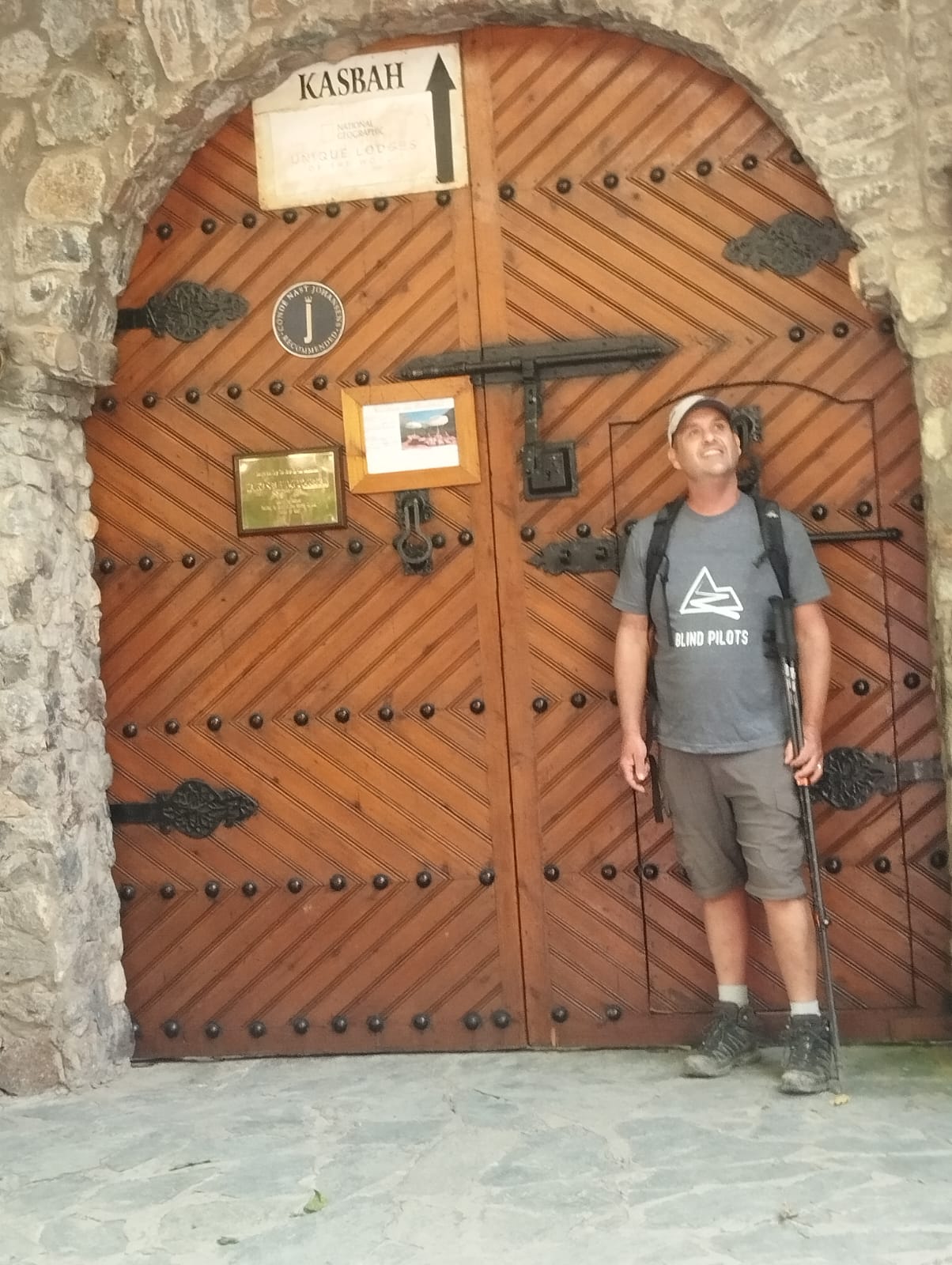 Man with hiking poles at large wooden doors with "KASBAH" sign
